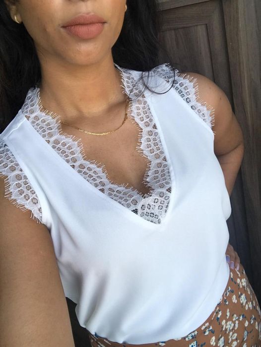 Reviewer in a sleeveless white top featuring lace trim, accessorized with a delicate gold necklace