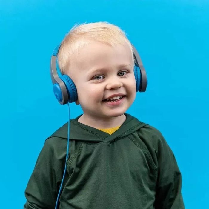 A child in a green shirt smiles while wearing headphones, set against a blue background
