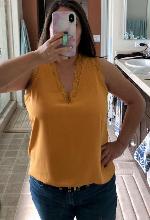 Person capturing a mirror selfie in a yellow sleeveless top with lace accents and jeans, set in a bathroom