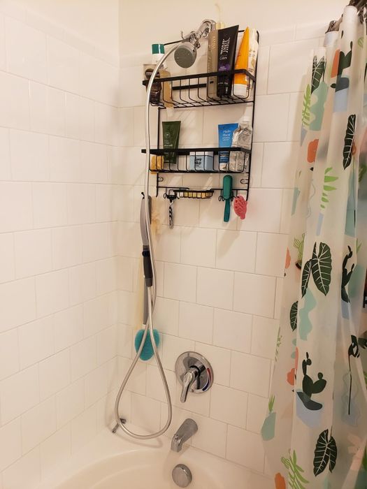 A reviewer’s shower setup with the grooming tool hanging from a suction cup on the wall