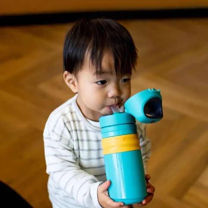A child in a striped long-sleeve shirt drinking from a turquoise and yellow sippy cup with a straw