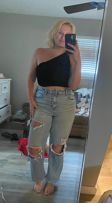 Reviewer capturing a mirror selfie in a black asymmetrical top and light-wash distressed jeans