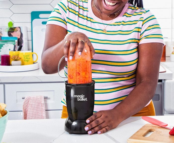 A person preparing a smoothie using a Magic Bullet blender in a cozy kitchen setting