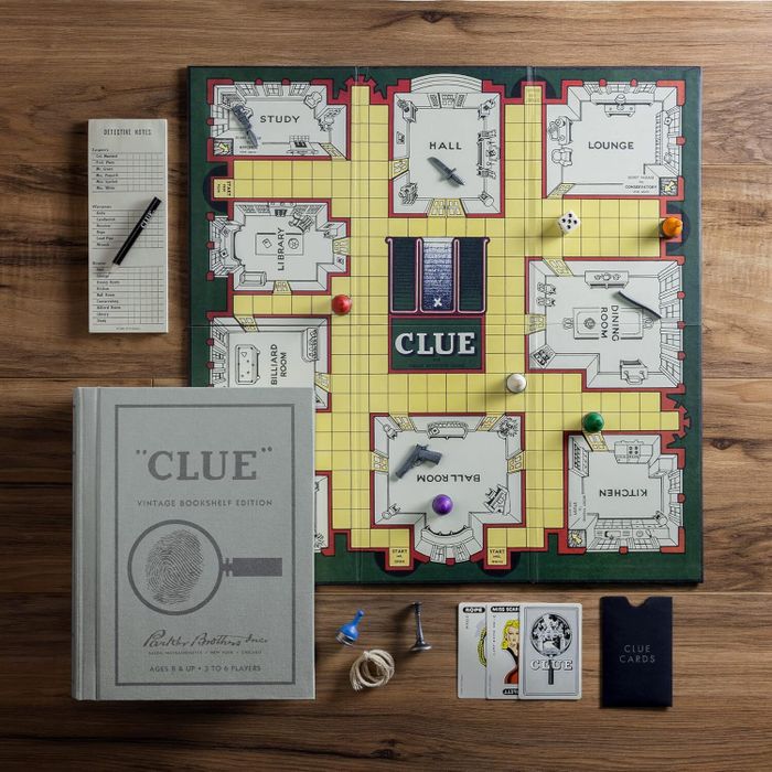 Clue board game arranged with pieces, dice, cards, a notepad, a pencil, and the Clue Vintage Bookshelf Edition box