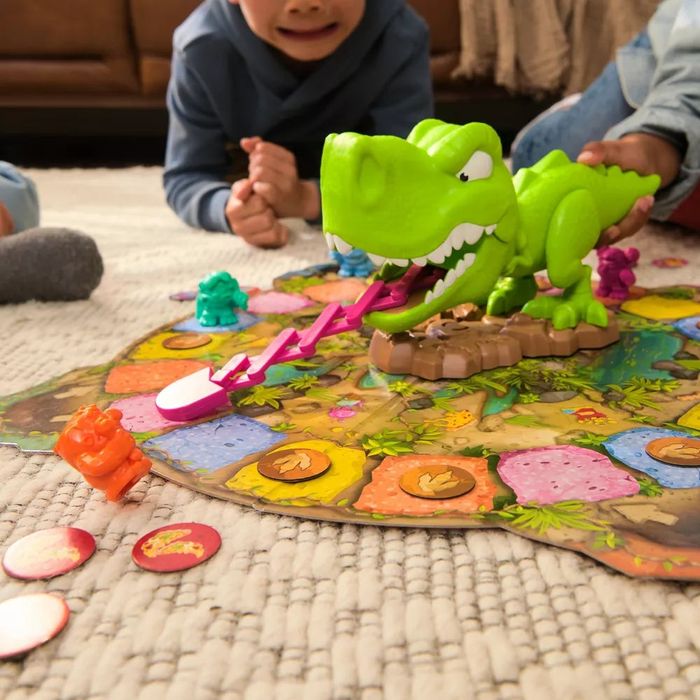 Kids playing a dinosaur-themed board game featuring a green dinosaur figure on a vibrant game board, surrounded by various game pieces