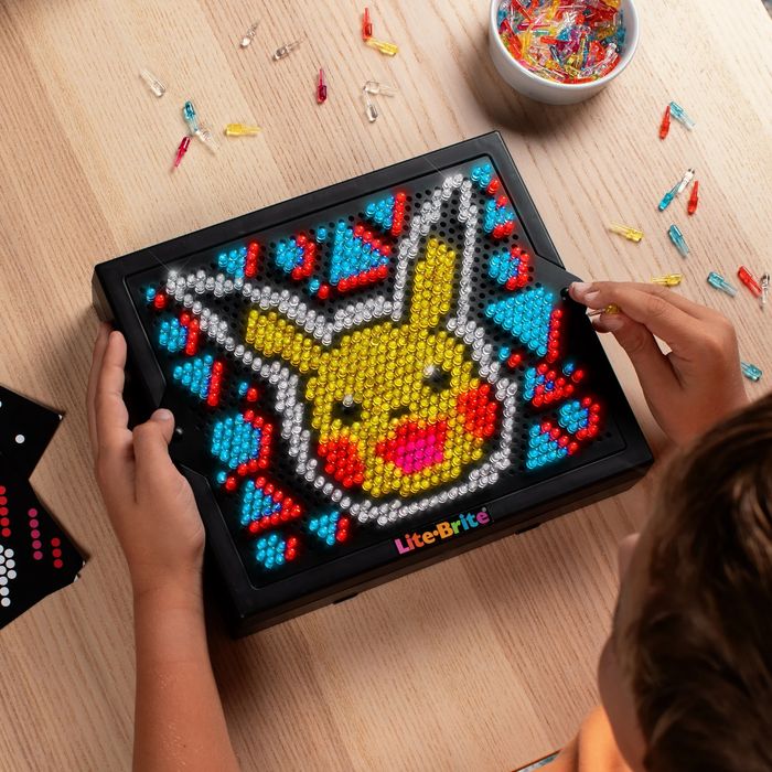 A child crafting a Pikachu design on a Lite-Brite toy, surrounded by colorful pegs on a table