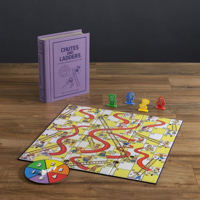 Chutes and Ladders board game set showcasing a board, spinner, and four colorful game pieces beside a purple book titled "Chutes and Ladders: Vintage Children's Edition."