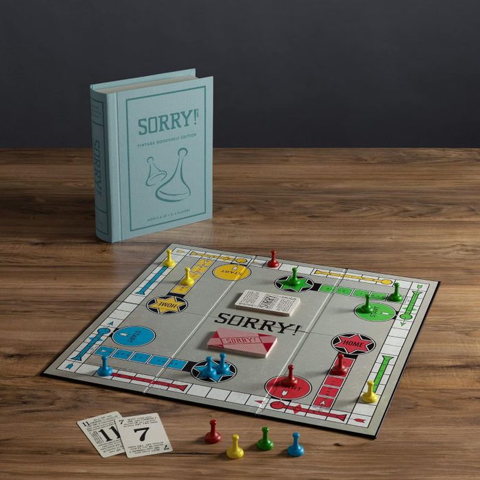 Sorry! board game set displayed on a wooden table, with the game box behind the board, and colorful pieces in yellow, blue, red, and green placed on the board