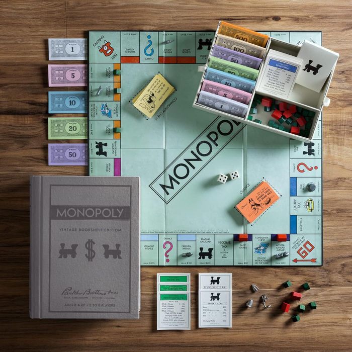 Monopoly Vintage Bookshelf Edition game set displayed on a wooden table, showcasing the board, money, cards, dice, houses, hotels, and storage case