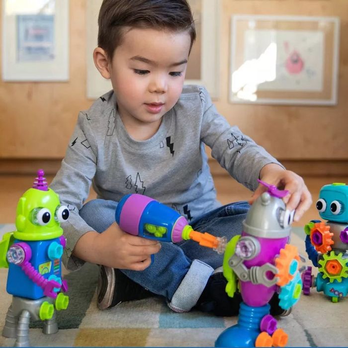 A young child sits on the floor, using a toy drill to put together colorful robot parts. The text below reads, 