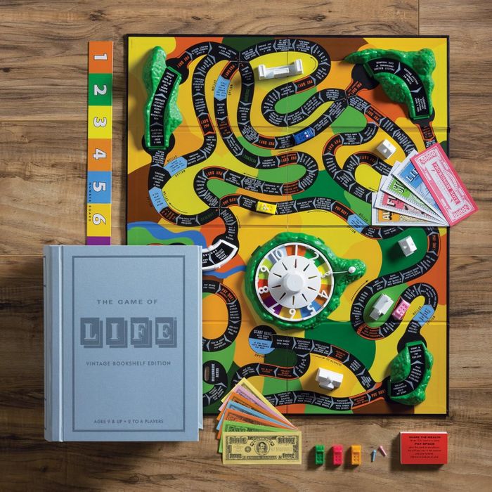 Board game setup displaying "The Game of Life: Vintage Bookshelf Edition" with the board, spinner, play money, cars, and instruction cards