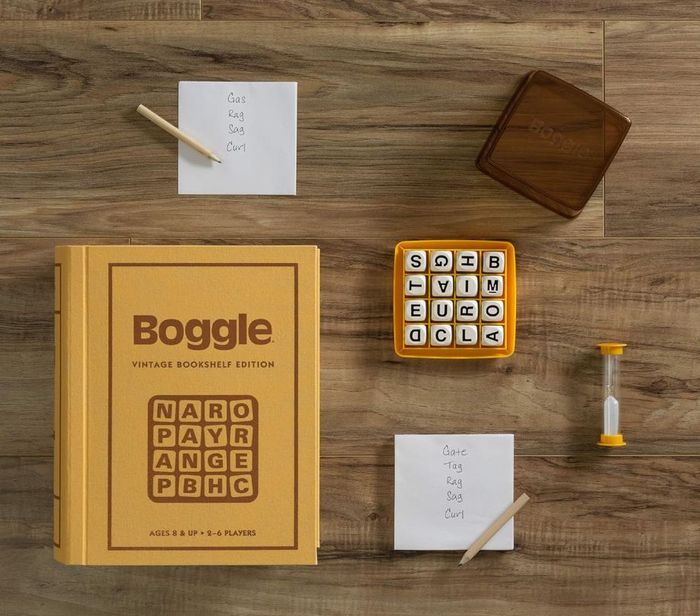 Boggle Vintage Bookshelf Edition game set, featuring a game book box, letter dice board, sand timer, notepad with "Gate, Rag, Sag, Curl" written, and a wooden stylus