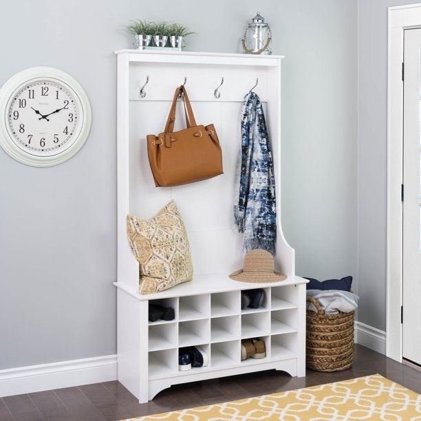 An entryway organizer with shoe storage, hooks holding a bag, scarf, pillow, and hat, complemented by a clock and decorative items above