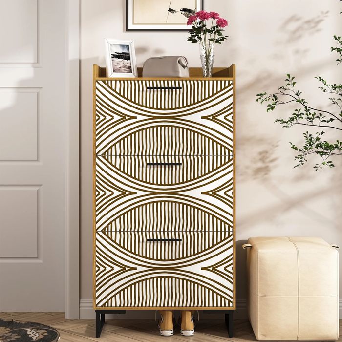 A modern dresser with a unique geometric pattern, featuring a photo frame and a vase of flowers, placed beside a beige ottoman in a chic room