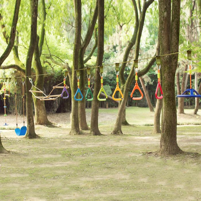 An outdoor obstacle course for children set among trees, featuring vibrant hanging rings and swings