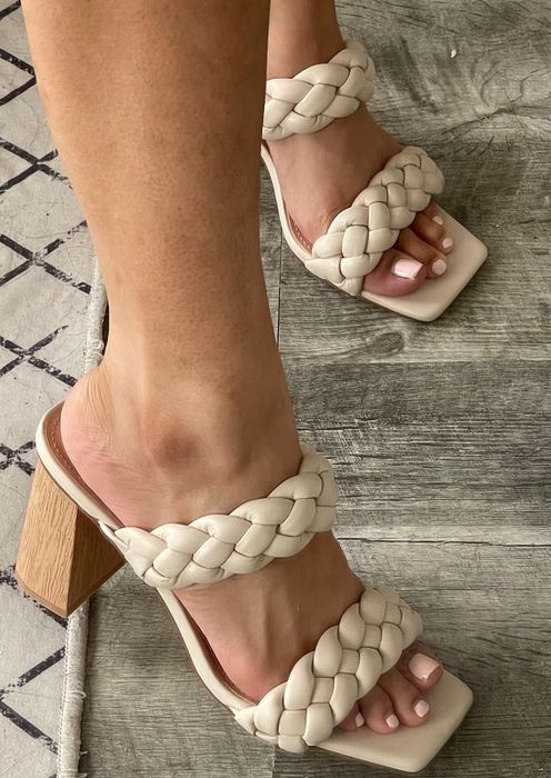 Close-up of feet wearing chic, braided-strap high-heeled sandals with painted toenails on a wooden floor