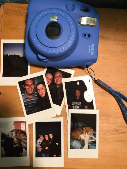 A reviewer's blue camera with small printed photos and a matching wrist strap.