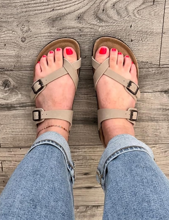 A person wearing sandals and blue jeans, with a view looking down at their feet