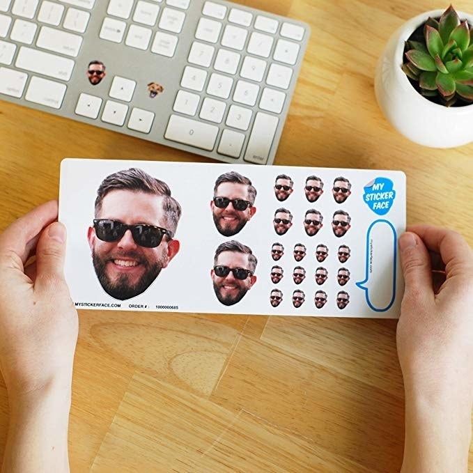 A sheet of stickers showcasing one small, two medium, six small, and 12 extra small stickers of a person's face, held in someone's hands.