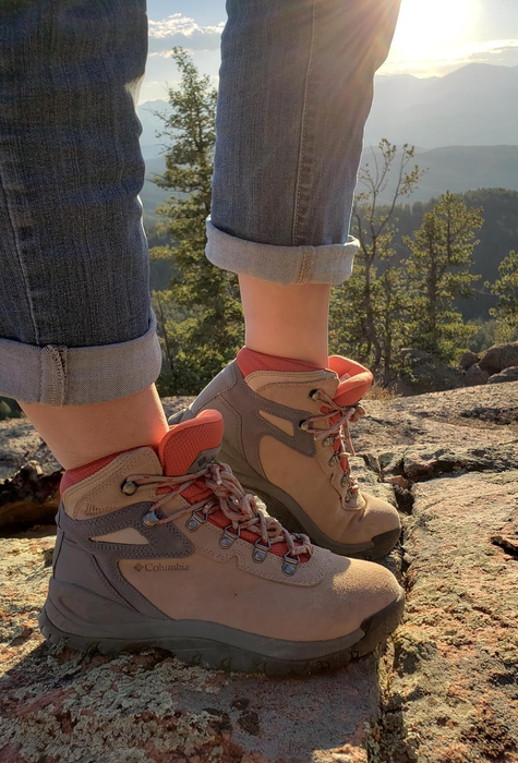 Person wearing hiking boots standing on a rocky overlook with a scenic mountain view