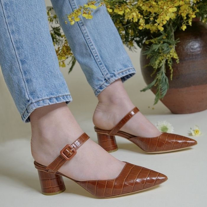 a model wearing jeans and brown crocodile-embossed leather mules