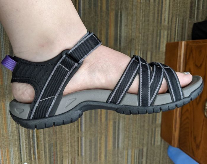 A photo of a reviewer’s foot wearing the black Teva sandal with gray trim, shown in profile view