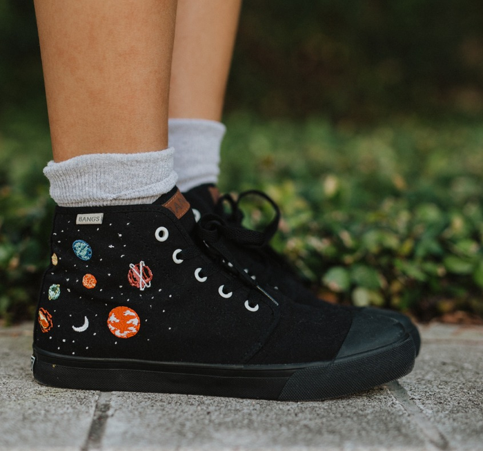 a model wearing black high-top canvas sneakers adorned with planetary embroidery