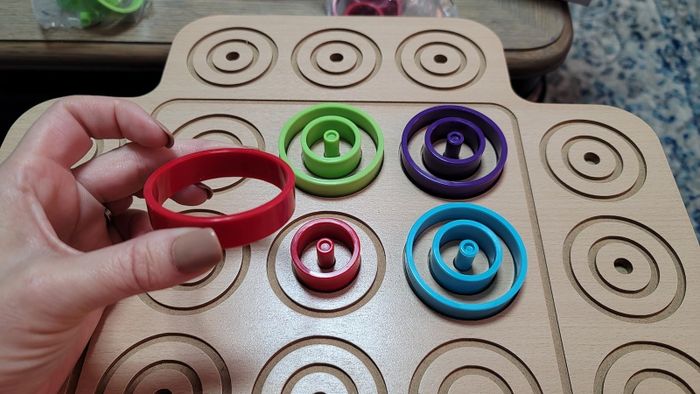 A reviewer's hand is holding a red circular piece above the game board in the image.