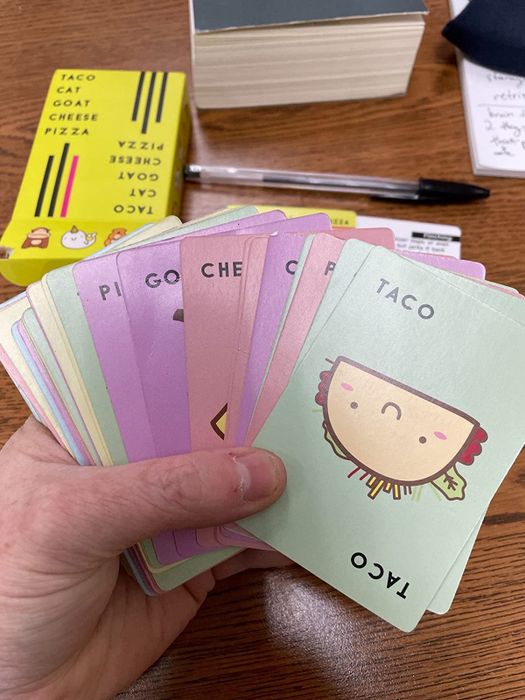 A close-up of a reviewer's hand holding a set of Taco Cat Goat Cheese Pizza cards.