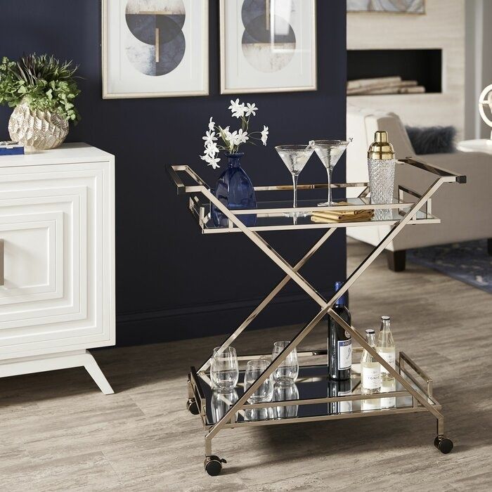 The two-tier rolling cart features mirrored shelves connected by crisscrossing light gold beams and handles.