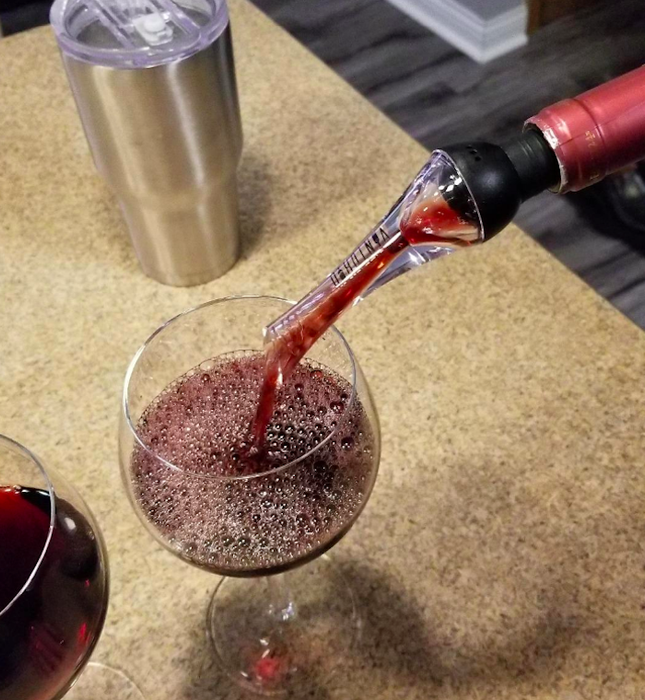 A wine bottle with the aerator attached, pouring wine into a glass.
