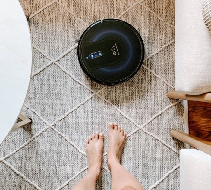 A reviewer’s perspective photo looking down at their feet with the robot vacuum on the carpet