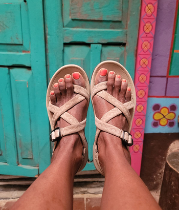 A person rocking thong sandals with crossed straps, standing on a colorful tiled floor.