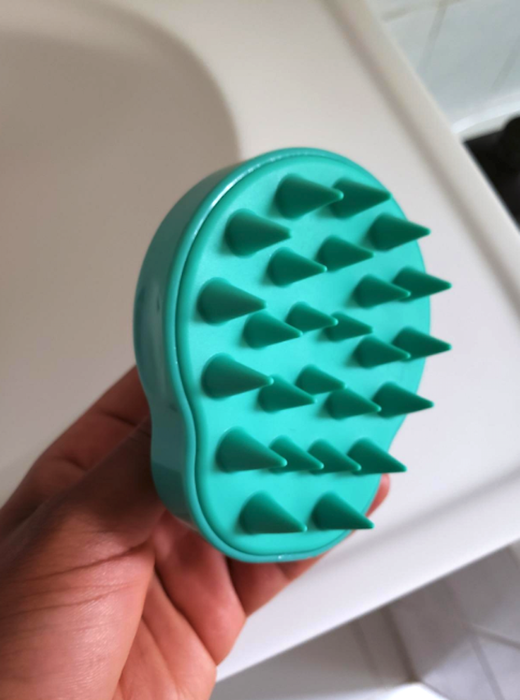 The reviewer is holding a scrubber equipped with soft rubber spikes, which are rounded at the tips to prevent pinching.