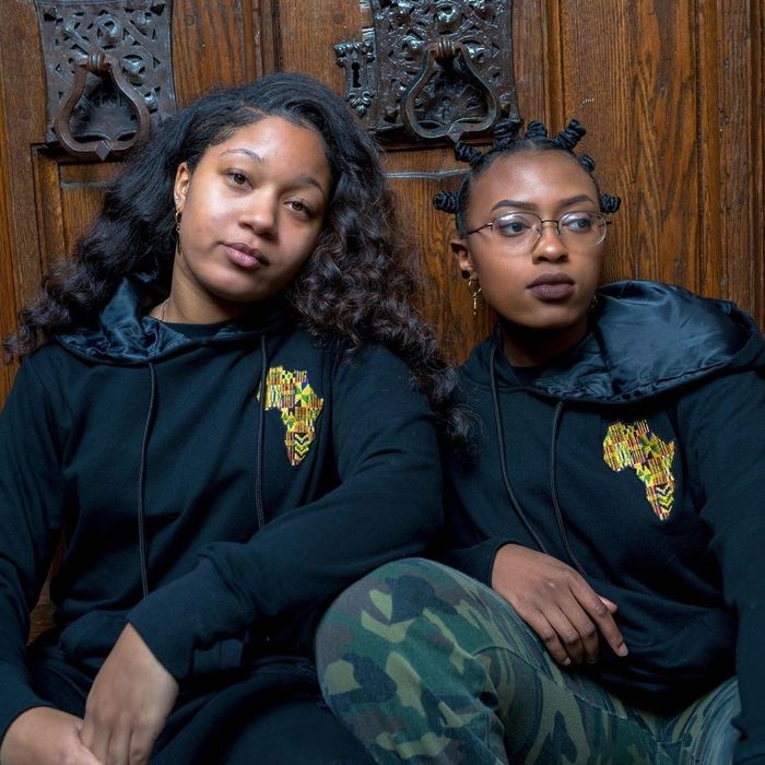two models rocking black hoodies with black satin-lined hoods and a vibrant Africa embroidery on the chest