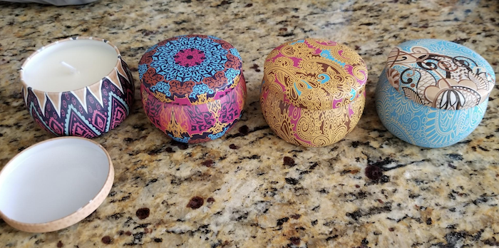 four candles in tin containers with lids resting on a reviewer's countertop