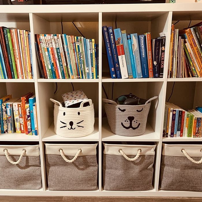 a white cat face basket and a gray dog face basket with handle designs resembling ears, placed on a child’s bookshelf