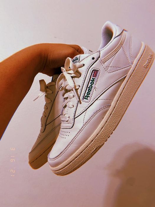 A reviewer holding up the off-white sneakers with a green Reebok label.