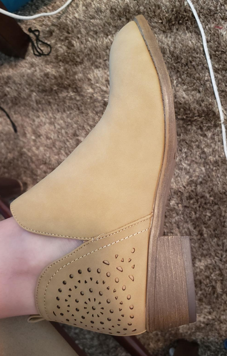 a reviewer wearing a light tan ankle boot with a short block heel and cutouts along the back heel
