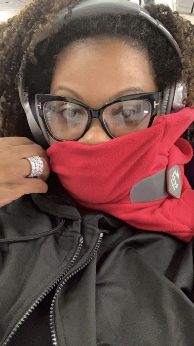 A reviewer sits on a plane, wearing the scarf around their neck, with half of their face covered.
