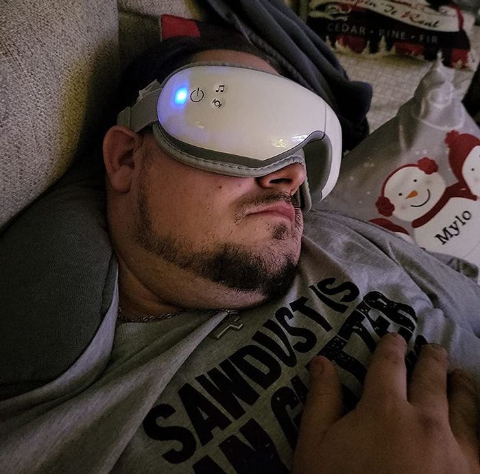 A reviewer dozing off on the couch with the heated eye massager on their face