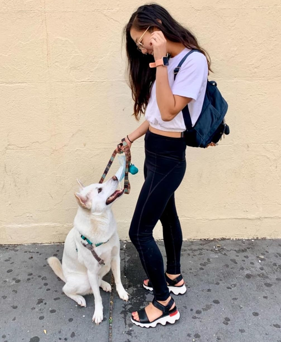 A photo of a person standing with their dog, dressed in black and white sandals, showcasing a casual yet stylish look.