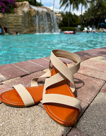 A reviewer’s beige sandals placed in front of a pool.