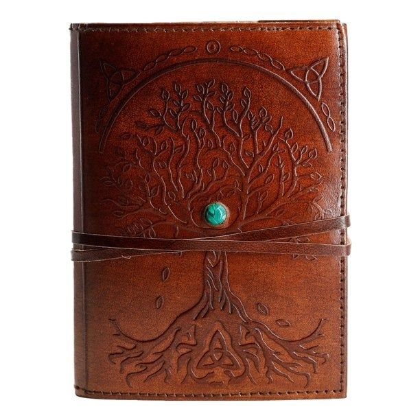 The front of the journal showcasing a tree of life design with a green gem at the center and leather wrap-around bands