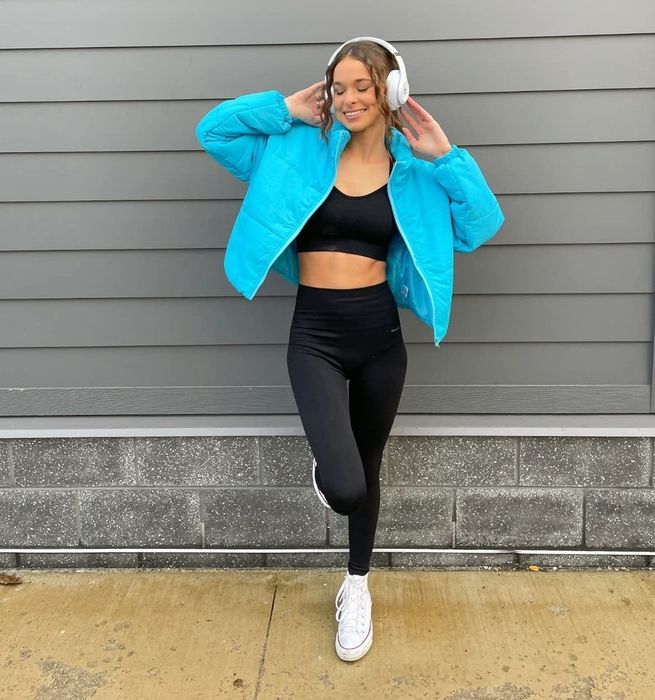 A reviewer standing outdoors in athletic attire, wearing white headphones