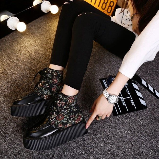 A model sitting, showcasing the flatform shoes from the side. The shoes lace up and reach just above the ankle.