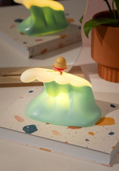 a lamp shaped like a wave with a tiny potato in swim trunks surfing on it