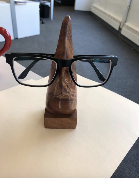 a reviewer's glasses resting on a wooden sculpture of a nose, which serves as the eyeglass holder