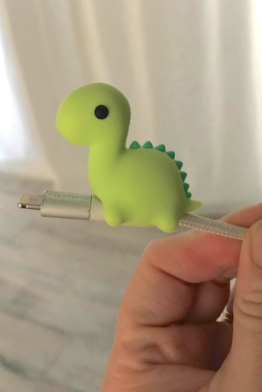 close-up of a green dinosaur-shaped cable bite placed on a phone or laptop charger