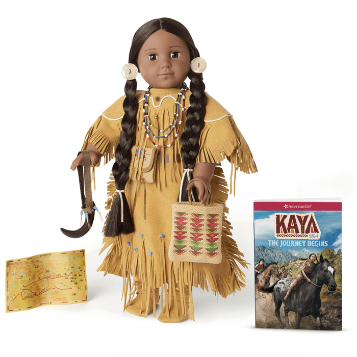 A Kaya doll dressed in traditional Indigenous attire, accompanied by accessories, a book, and a map